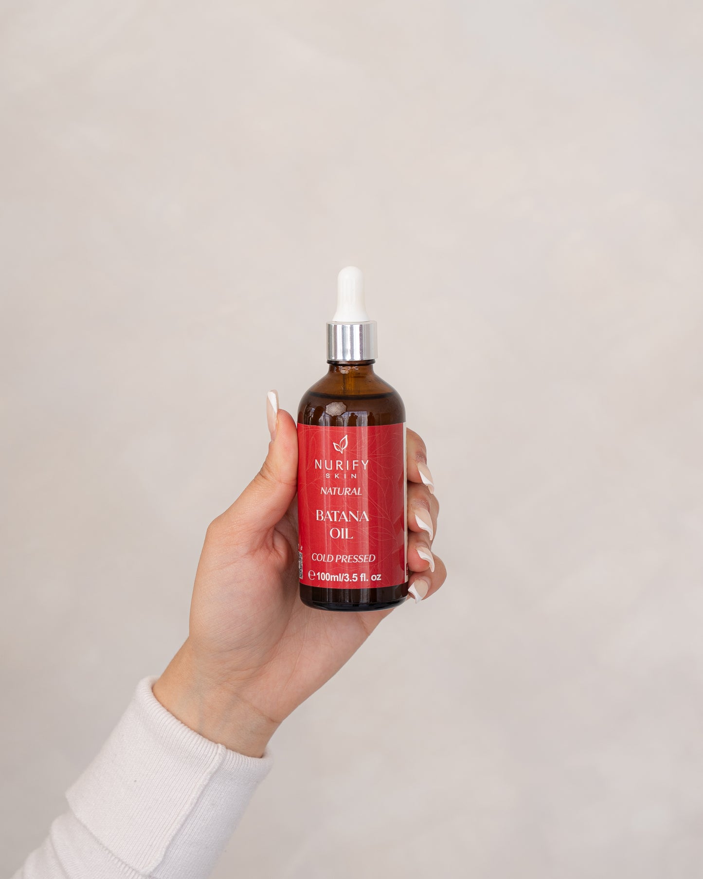 Batana Oil Bottle in the hand of a model on a minimal background.