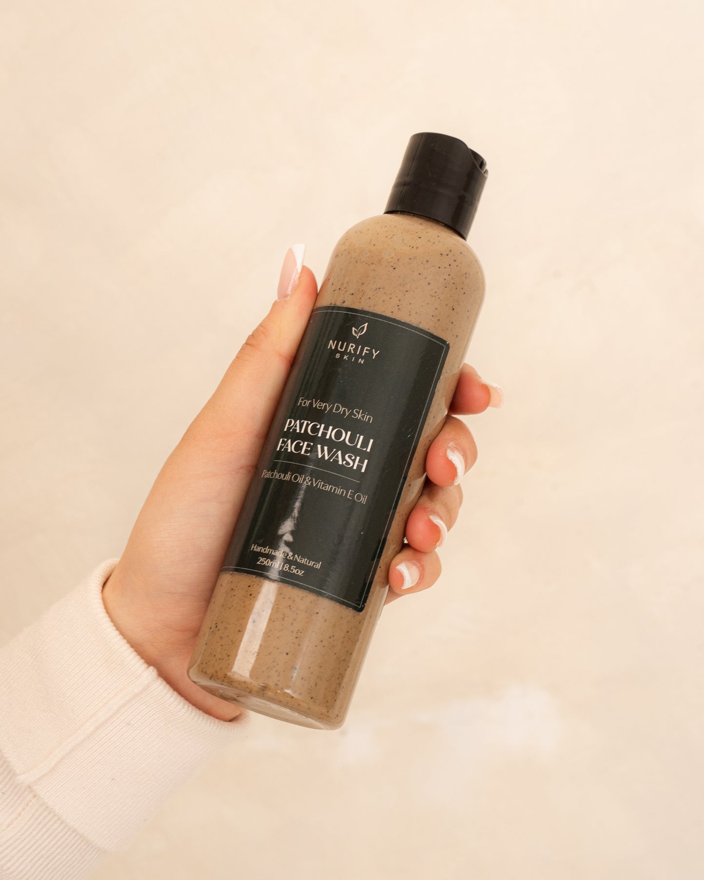 Patchouli Face Wash on a minimal background in the hand of a model, green label for eczema, dermatitis, and dry skin.