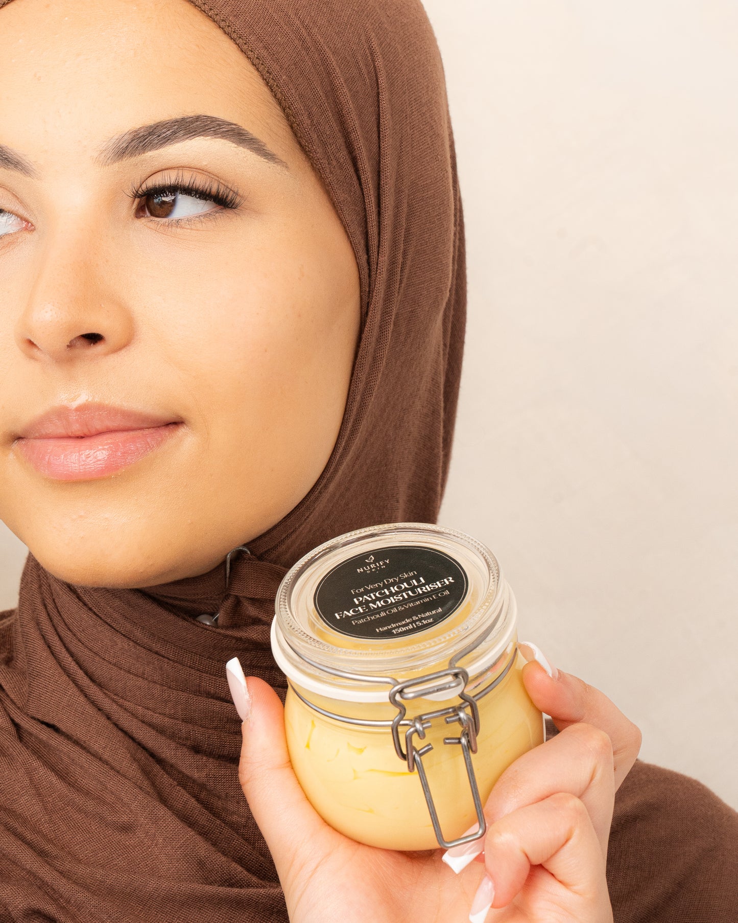 Patchouli Face Moisturiser on a minimal background in the hand of a model, green label for eczema, dermatitis, and dry skin.