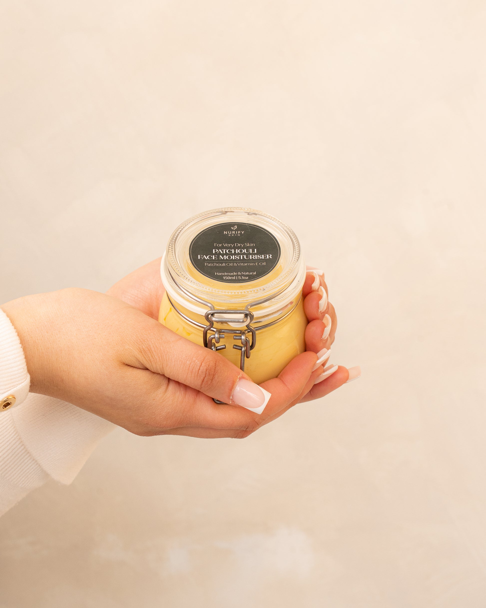 Patchouli Face Moisturiser on a minimal background in the hand of a model, green label for eczema, dermatitis, and dry skin.