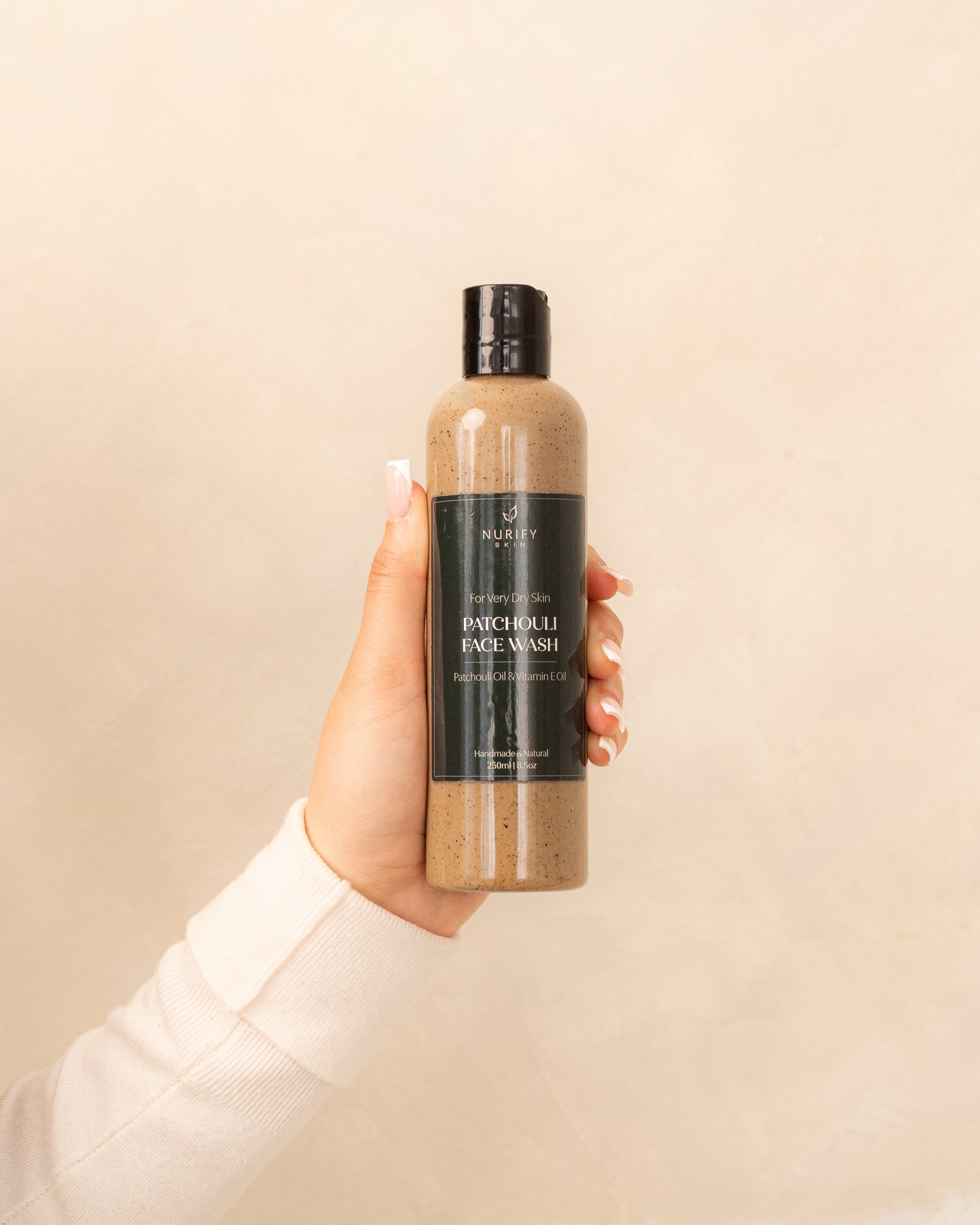 Patchouli Face Wash on a minimal background in the hand of a model, green label for eczema, dermatitis, and dry skin.
