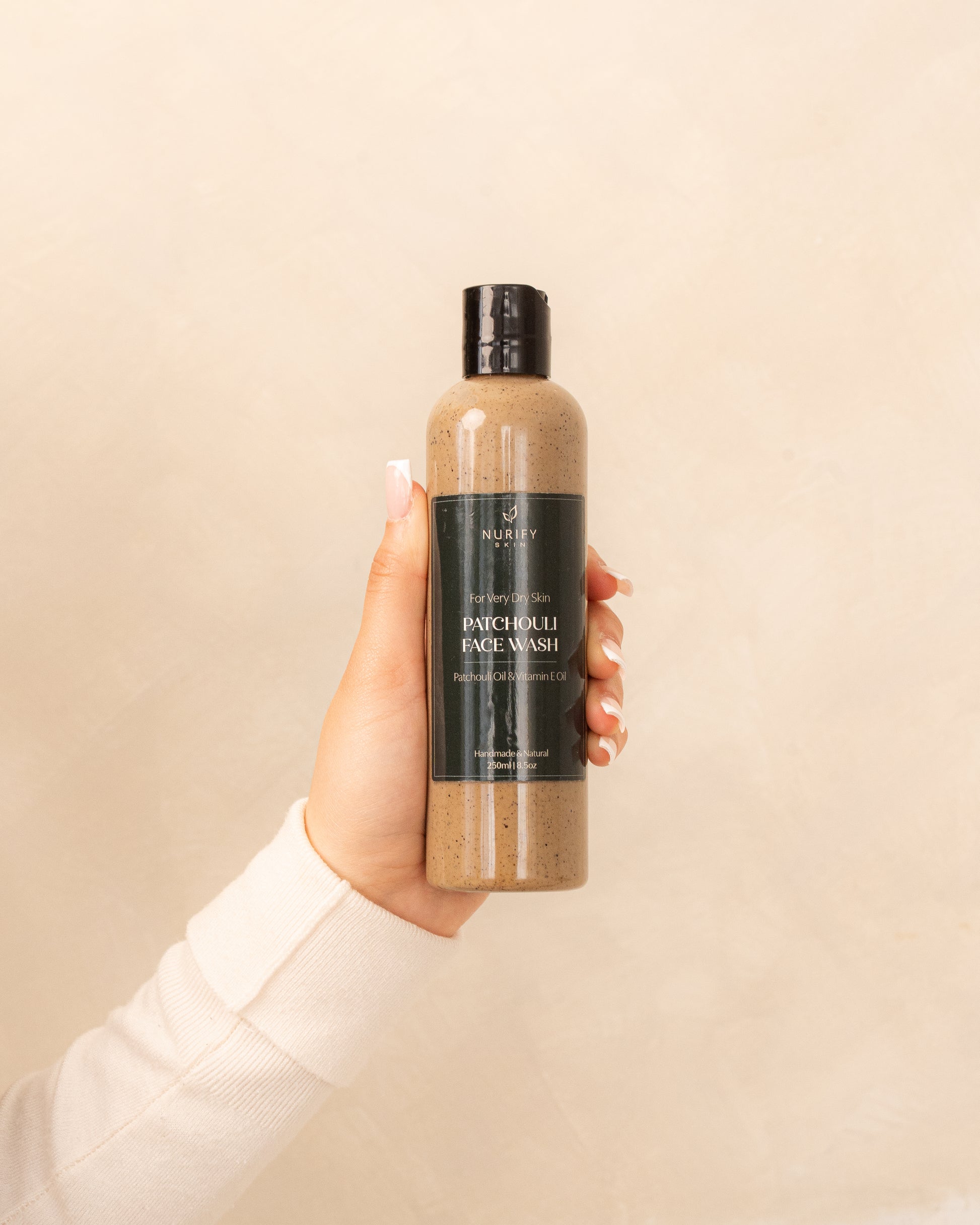 Patchouli Face Wash on a minimal background in the hand of a model, green label for eczema, dermatitis, and dry skin.