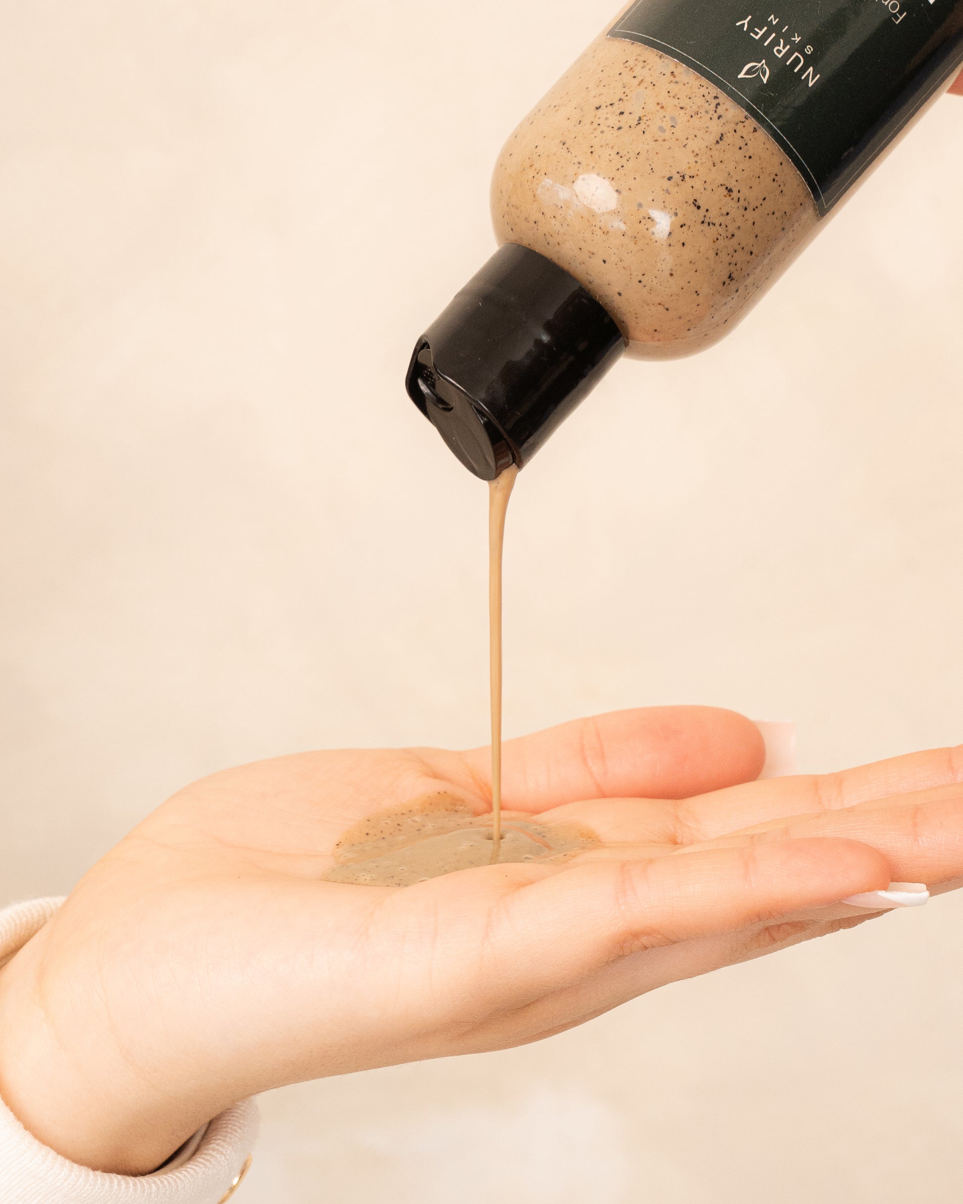 Patchouli Face Wash dripping out of the bottler on a minimal background on the hand of a model, green label for eczema, dermatitis, and dry skin.