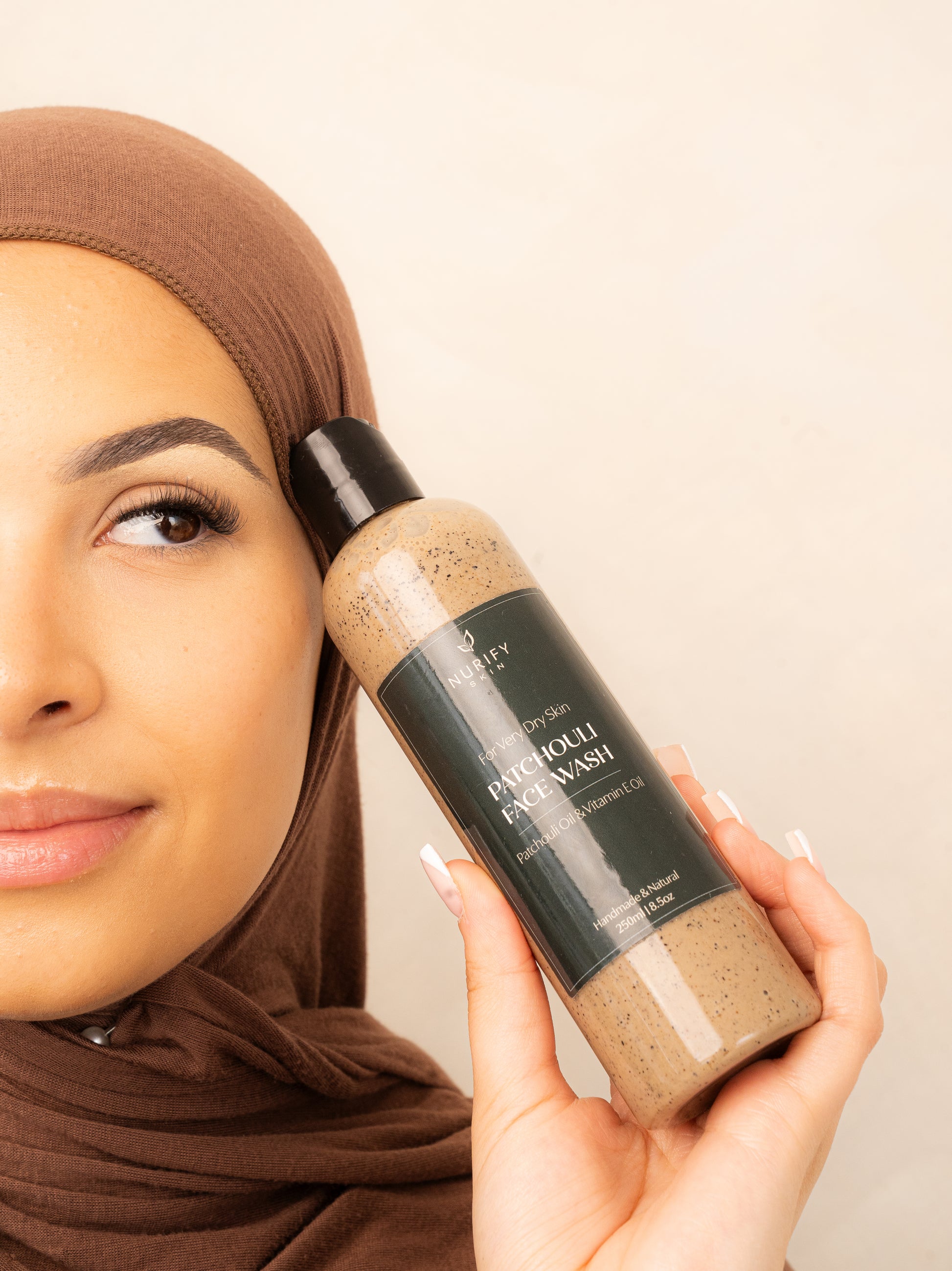 Patchouli Face Wash on a minimal background in the hand of a model, green label for eczema, dermatitis, and dry skin.